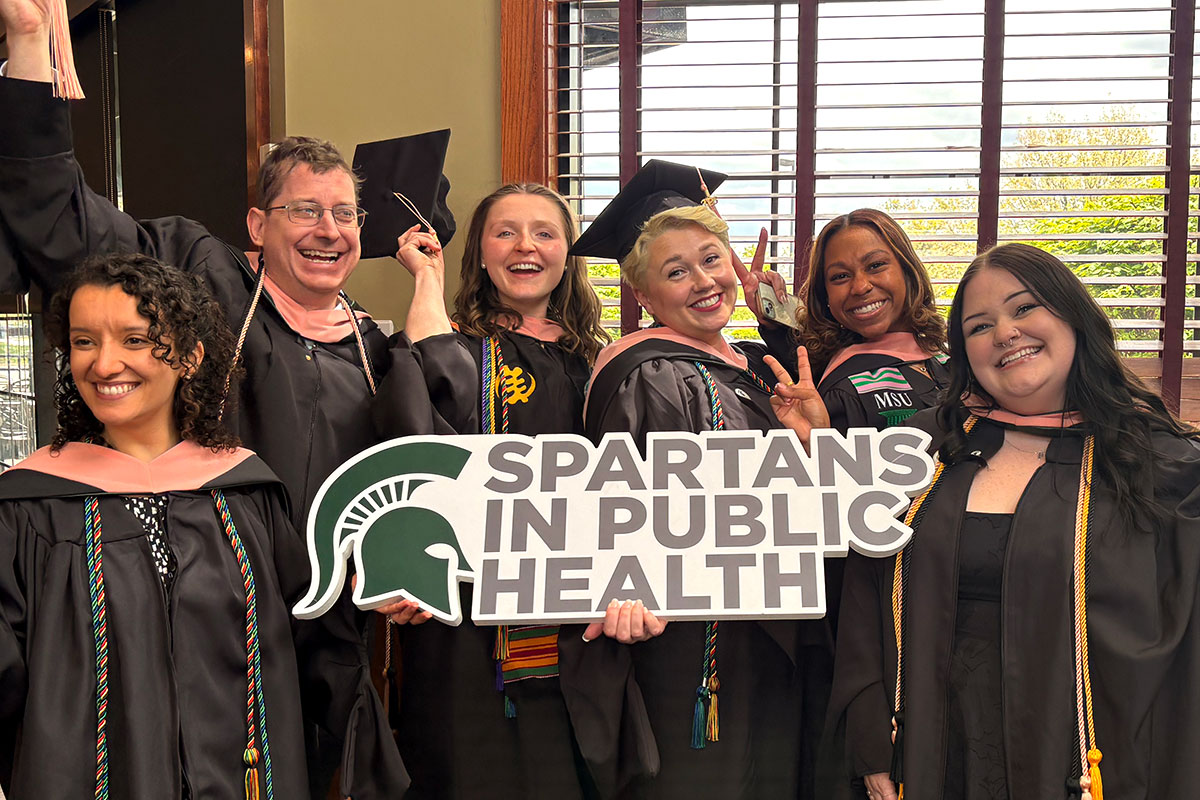 Graduates smiling and being playful while holding a Spartans In Public Health sign