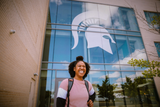 woman smiling in front of MSU glass window